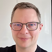 Ein Mann mit Brille und kurzen Haaren lächelt freundlich in die Kamera. Hintergrund ist hell und neutral.